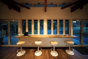 Un espace bar avec un comptoir en bois et quatre tabourets, de grandes fenêtres et une vue sur l’extérieur.