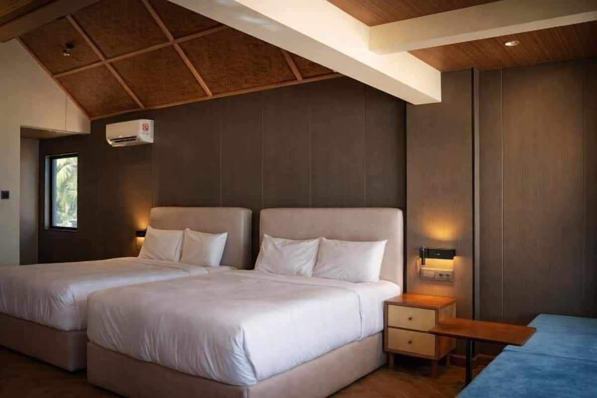 A bedroom with two beds, a nightstand, and a wooden ceiling.