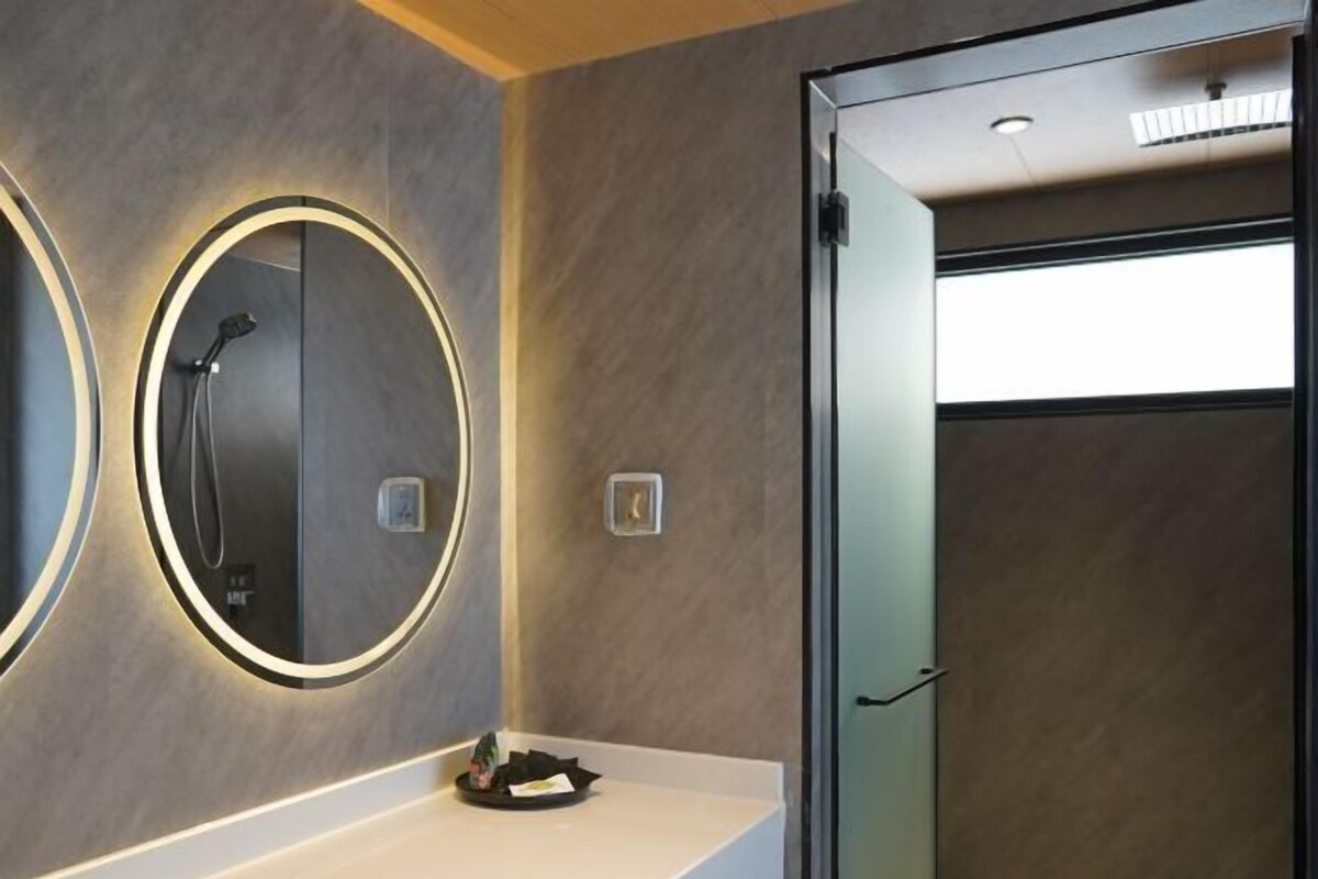 Un baño moderno con dos espejos grandes, una ducha y una puerta de vidrio que da a otra habitación.