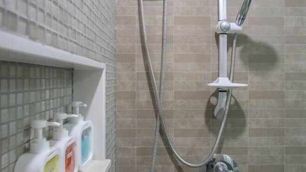 Egy zuhanyzó, amely kézi zuhanyfejet, zuhanycsövet és a falra szerelt vezérlőcsapot tartalmaz.