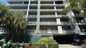A multi-story building with balconies, a covered parking area, and a green hedge. - Roxpresso Nimman 15 (Chiang Mai)