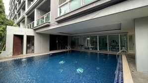A swimming pool adjacent to a building with balconies and large windows. - Roxpresso Nimman 15 (Chiang Mai)