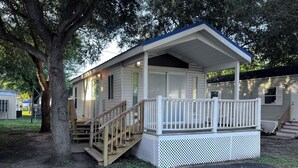 A single-story cabin with a porch, wooden steps, and a fenced deck area. - The Shady Oaks, with Pool Access! (Harlingen)
