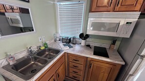 A kitchen with wooden cabinets, a double sink, a microwave, and a refrigerator. - The Shady Oaks, with Pool Access! (Harlingen)