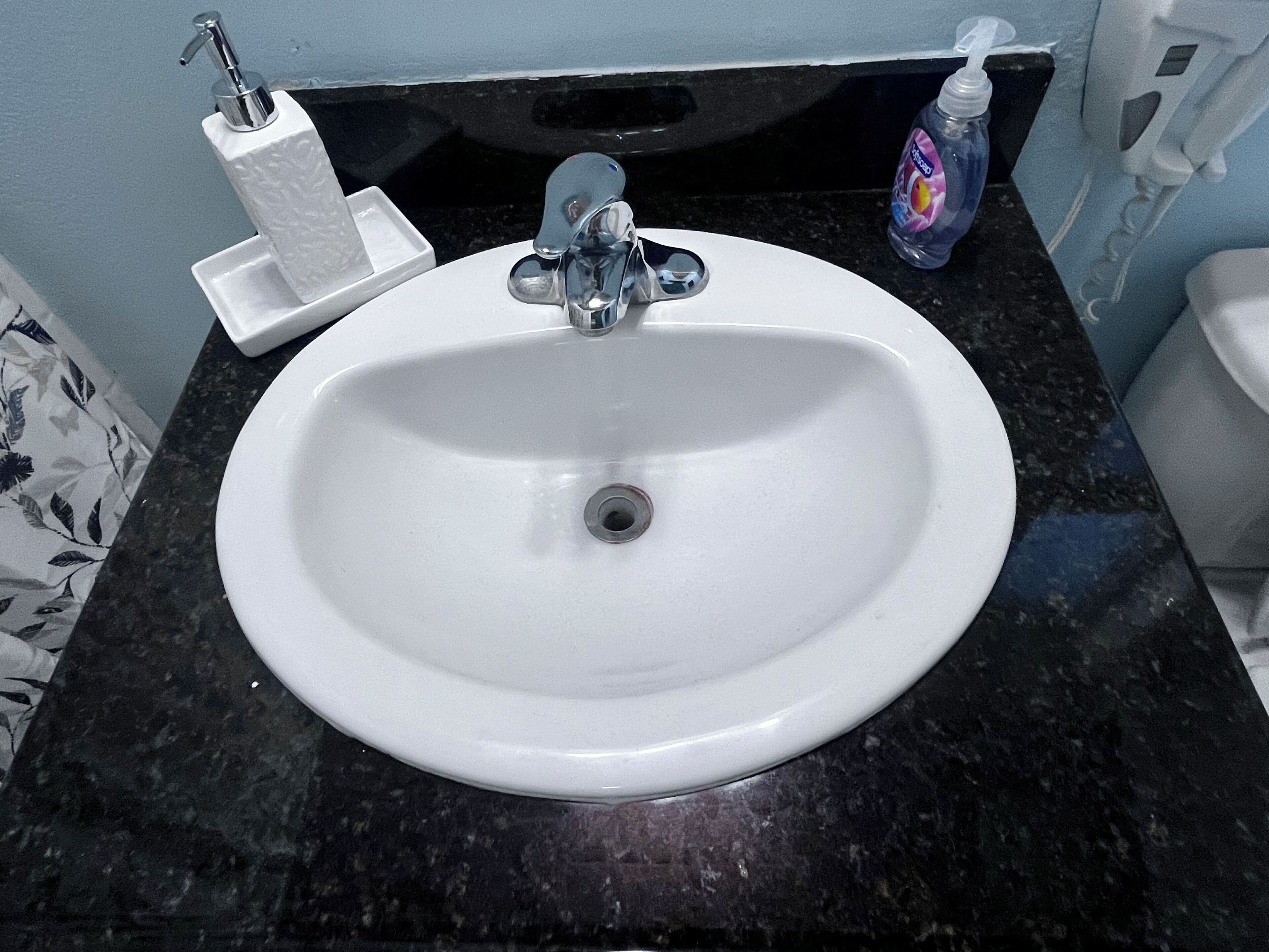 Un lavabo con grifo cromado, dispensador de jabón y soporte para papel higiénico sobre una encimera oscura.