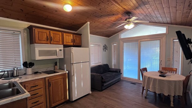 A compact kitchen with wooden cabinets, a white refrigerator, a microwave, and a dining area with a table and chairs. - The Shady Oaks, with Pool Access! (Harlingen)