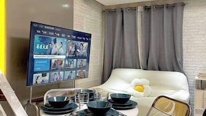 A modern living room with a white sofa, a flat-screen TV mounted on the wall, and a dining table set with blue plates and glasses. - Thompson Suites High Street (Fort Victoria) (Taguig)