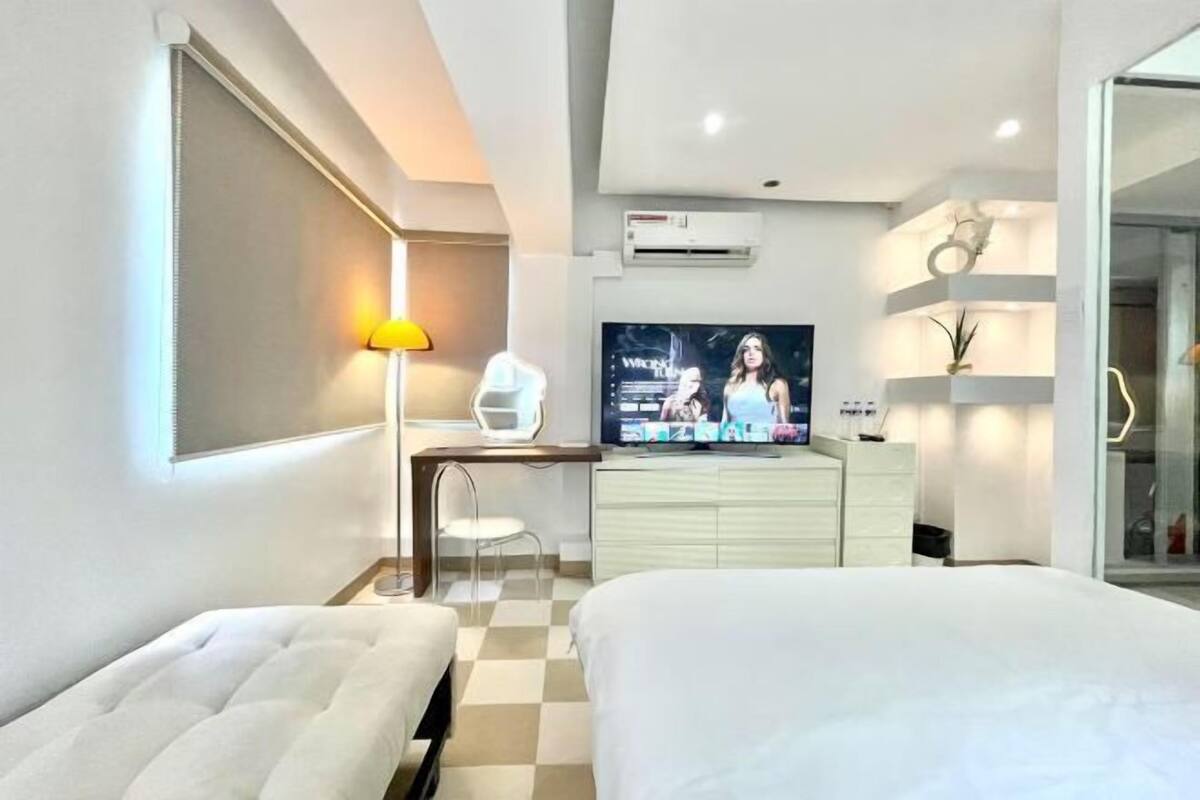 A modern hotel room with a bed, a desk with a chair, a TV, and a wardrobe.