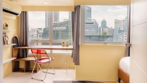 A modern hotel room with a large window, a desk, a chair, and a bed. - Thompson Suites High Street (Fort Victoria) (Taguig)