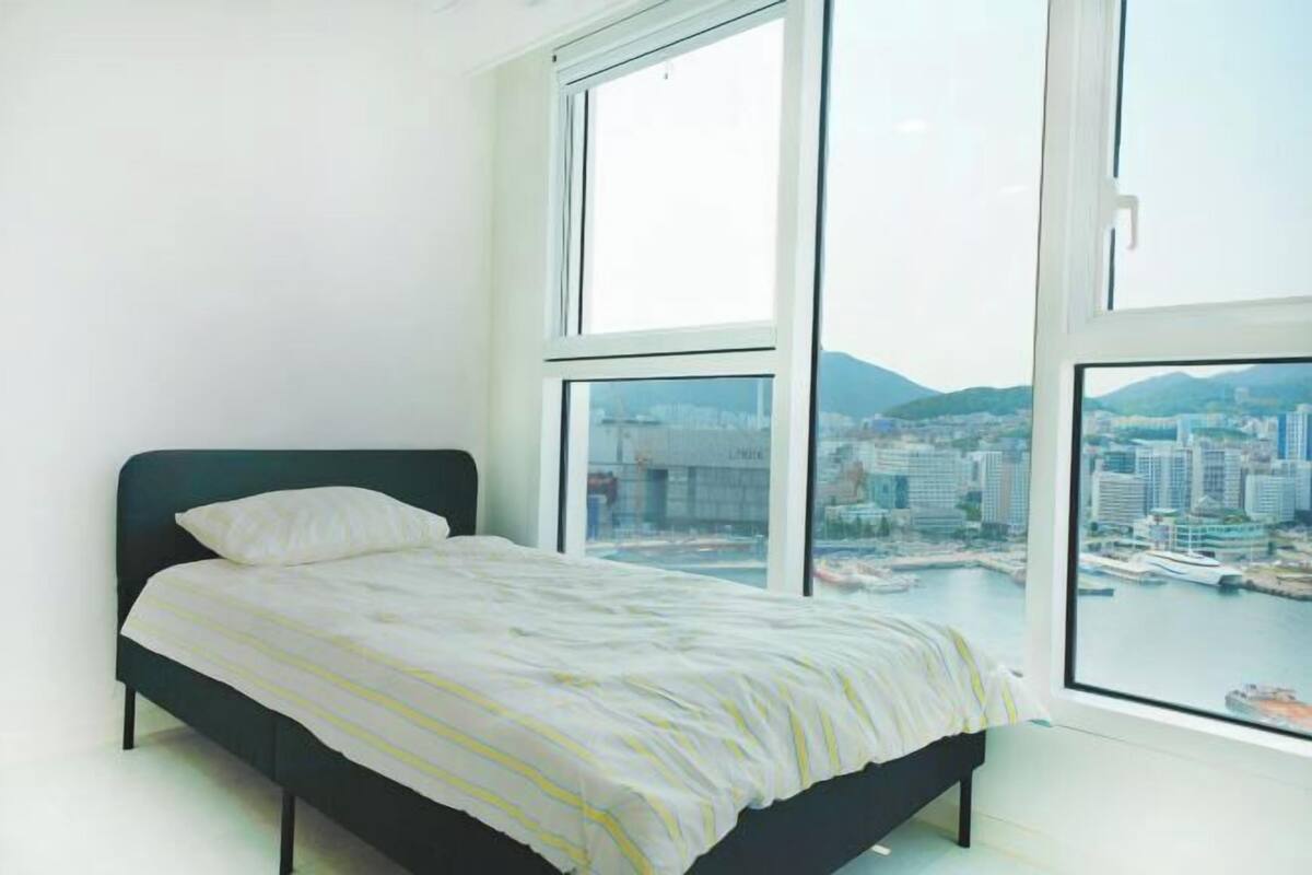 A bedroom with a bed, large windows, and a city view.