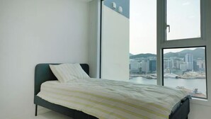 A bedroom with a bed, a large window, and a city view. - Busan Ocean Stay (Busan)