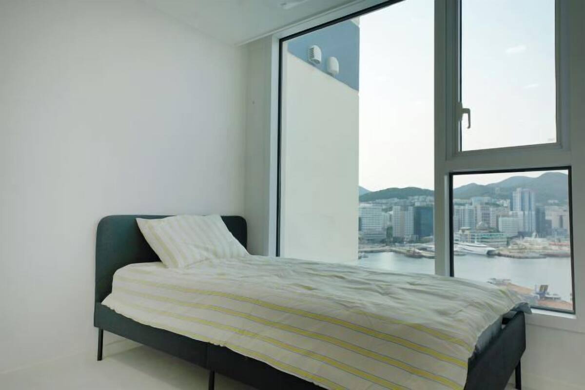 A bedroom with a bed, a large window, and a city view.