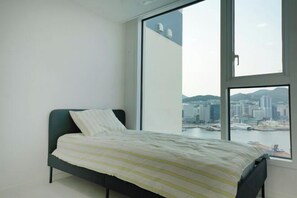 A bedroom with a bed, a large window, and a city view. - Busan Ocean Stay (Busan)