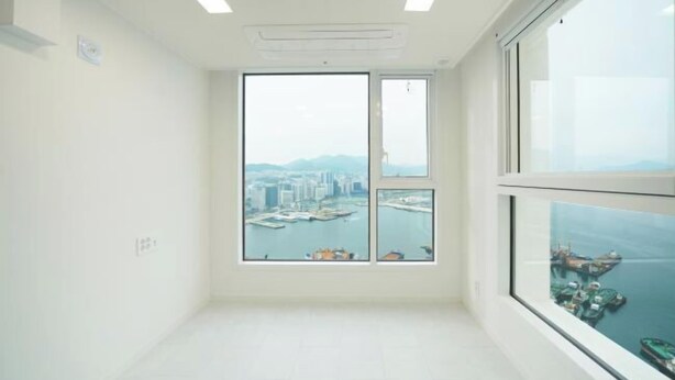 A room with a large window offering a view of a cityscape and water. - Busan Ocean Stay (Busan)