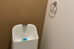 Um urinol branco com um dosador de sabonete azul, um porta-toalhas de metal e uma parede bege.