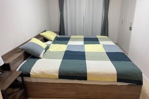 Uma cama bem arrumada com colcha xadrez, cabeceira de madeira e mesa de cabeceira com abajur.