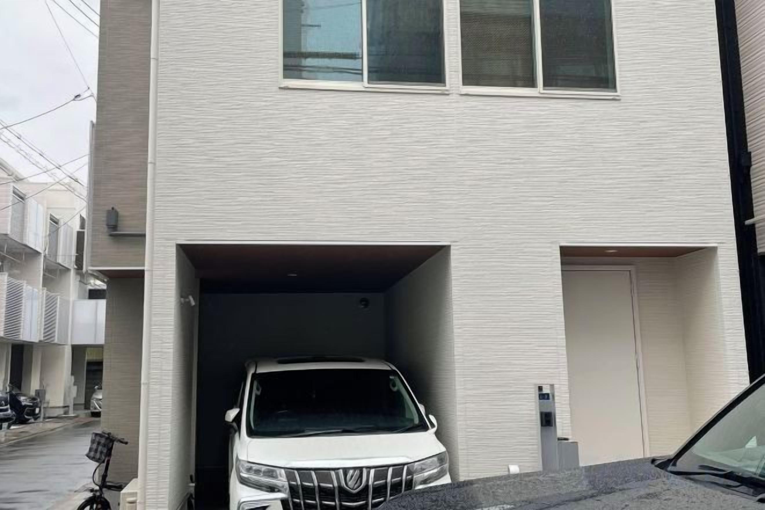 A white car parked in a garage attached to a building with a flat facade and a door on the right side.