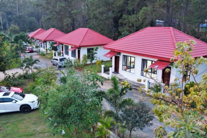 A row of white buildings with red roofs, surrounded by greenery and parked cars.