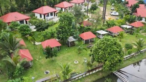 Un complexe hôtelier composé de plusieurs chalets aux toits rouges, entourés d’une végétation luxuriante et bordé par une rivière.