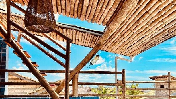 Eine Holztreppe führt zu einem Poolbereich mit Bambusdach und Blick auf Gebäude im Hintergrund.