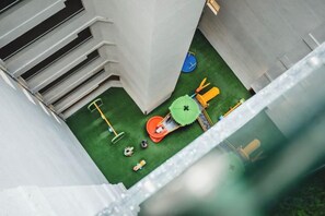 A narrow corridor with a small play area featuring a green artificial turf, a red toy car, and a yellow toy truck. - Beach Stay by Wahuj Maldives (Malé)