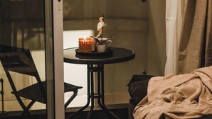 Una habitación con puerta de vidrio, una pequeña mesa con un adorno, una silla y una cama con manta.