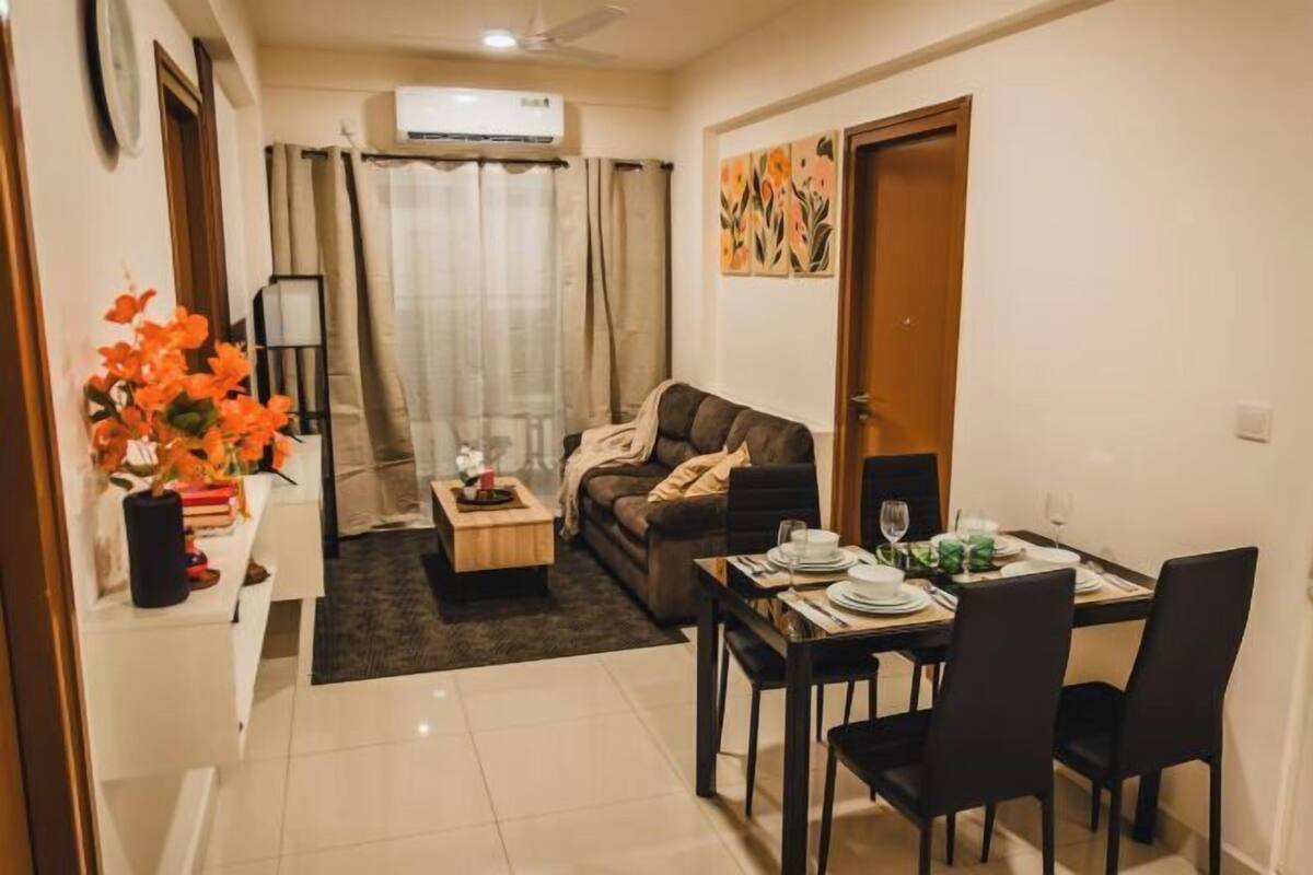 Un espacio habitable compacto con sofá, mesa de centro, mesa de comedor para cuatro personas y una mesita auxiliar con un jarrón de flores.