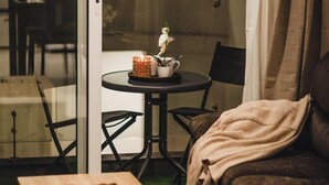 Una habitación acogedora con un vidrio que da a un balcón, una pequeña mesa redonda con una vela y una planta, y un sofá marrón.