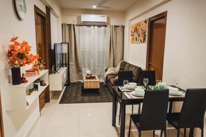 Una sala de estar moderna con un sofá, una mesa de comedor para dos personas, una mesa de centro y un televisor.
