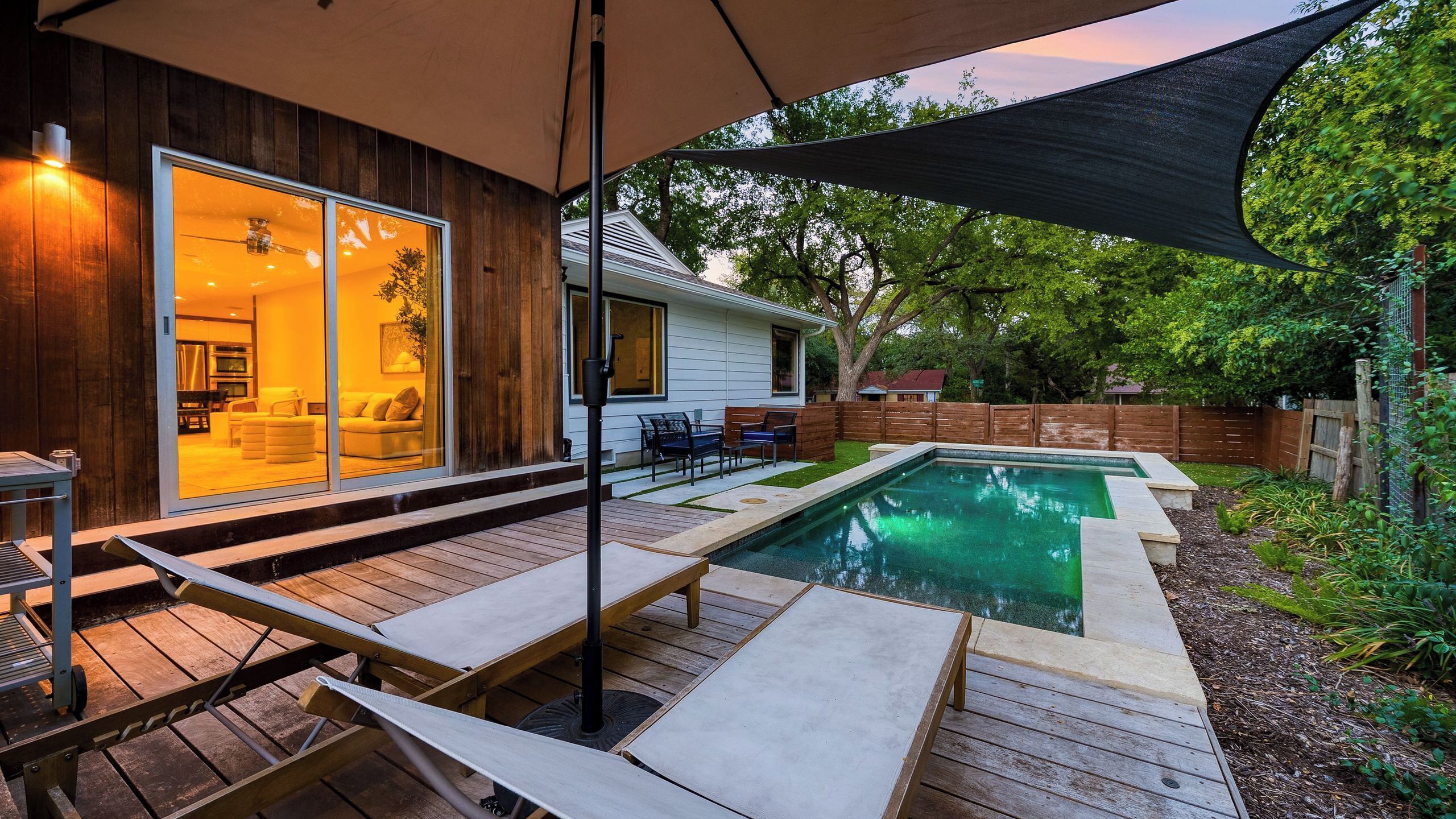 A backyard with a swimming pool, wooden deck, and a house with large windows.