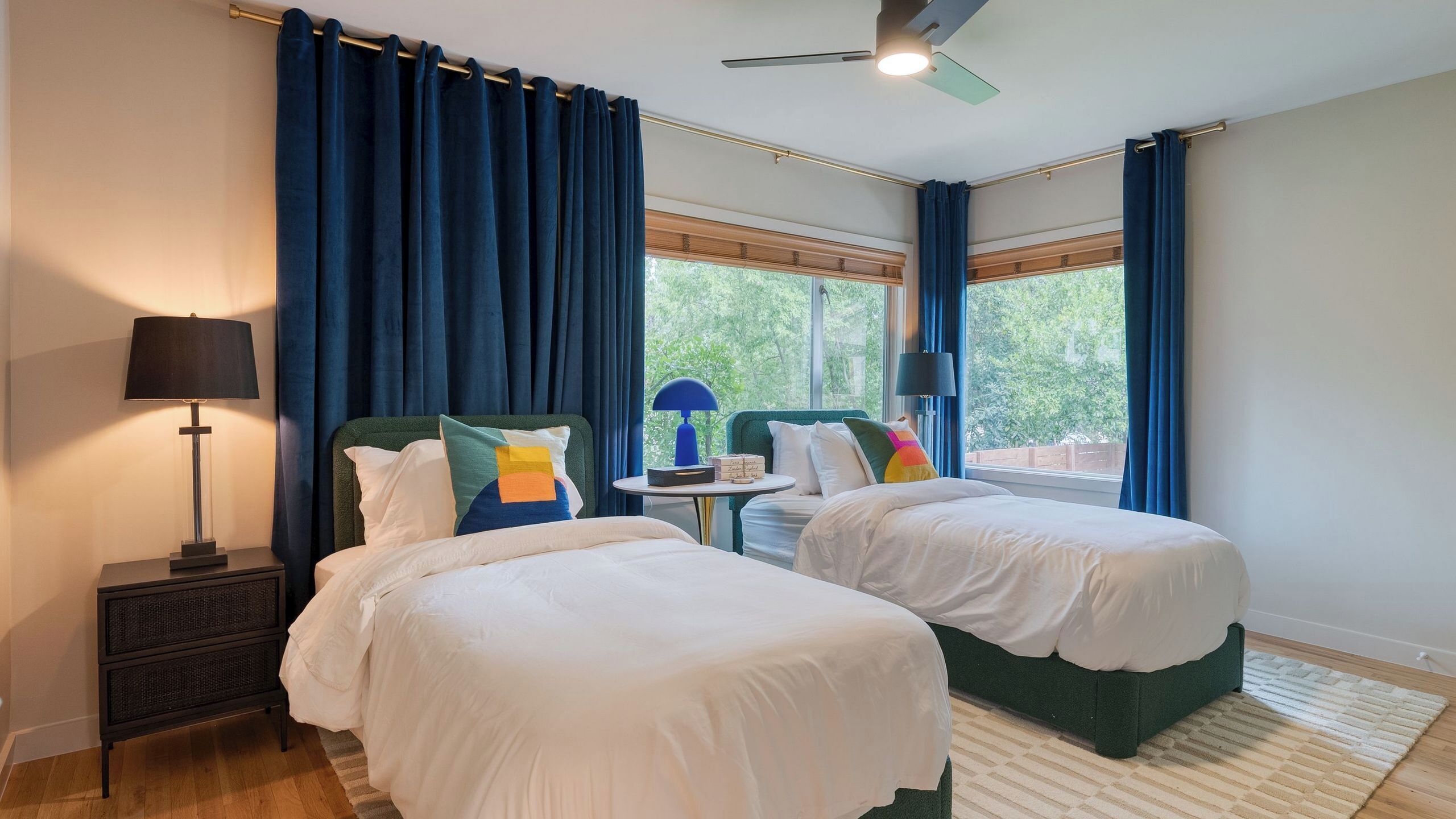 Une chambre d’hôtel avec deux lits, une table de chevet, une lampe, une petite table avec une lampe et une vue sur la verdure à l’extérieur.