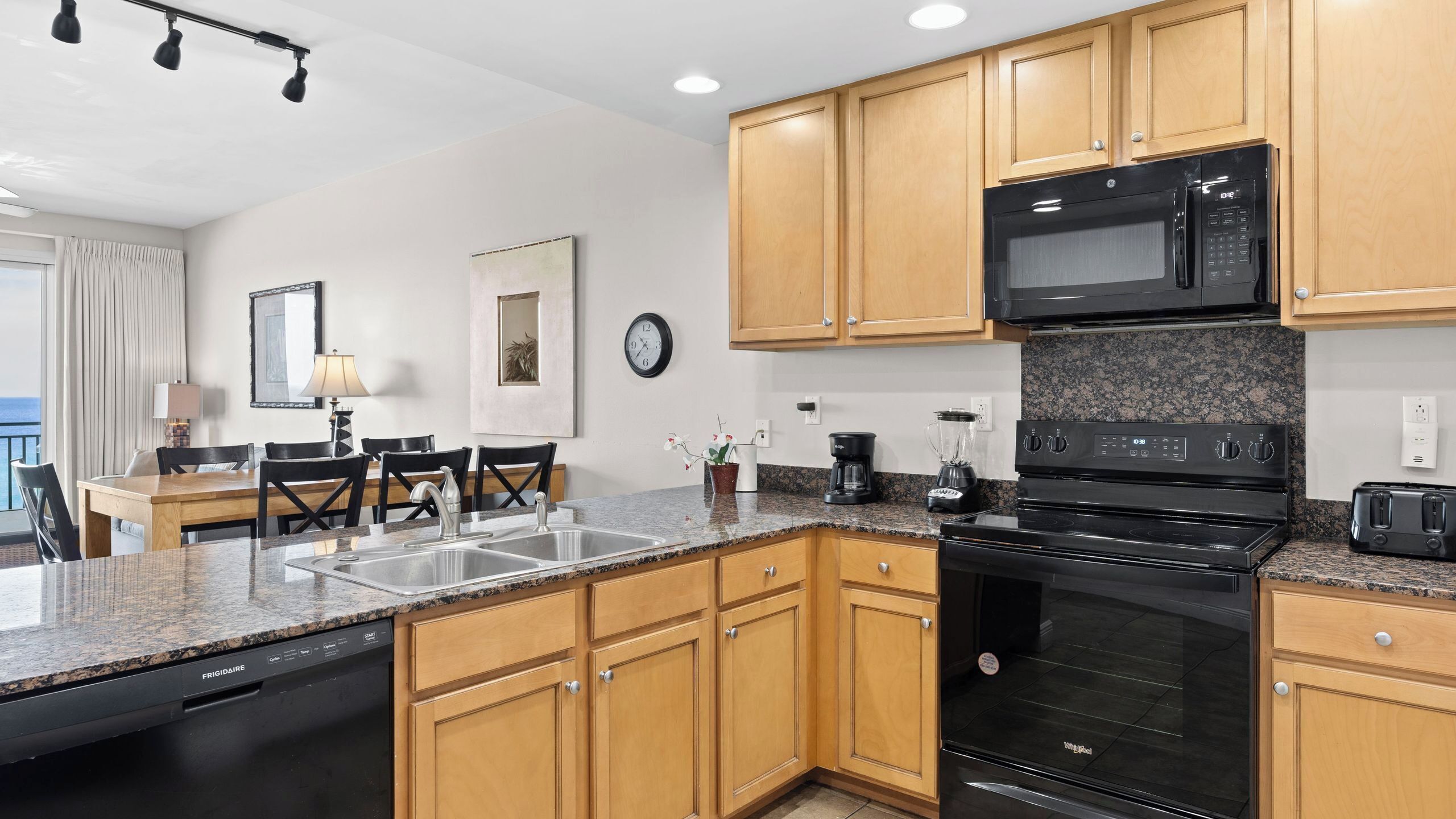 A modern kitchen with granite countertops, wooden cabinets, a built-in oven, a microwave, and a dishwasher.