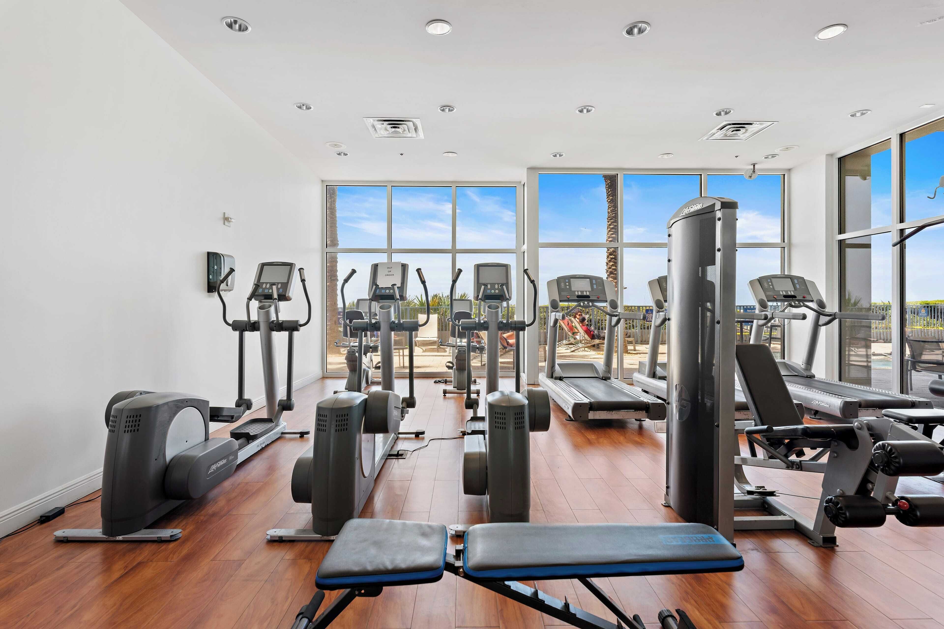 Un gimnasio con diverso equipo de ejercicio, amplias ventanas y suelo de madera.