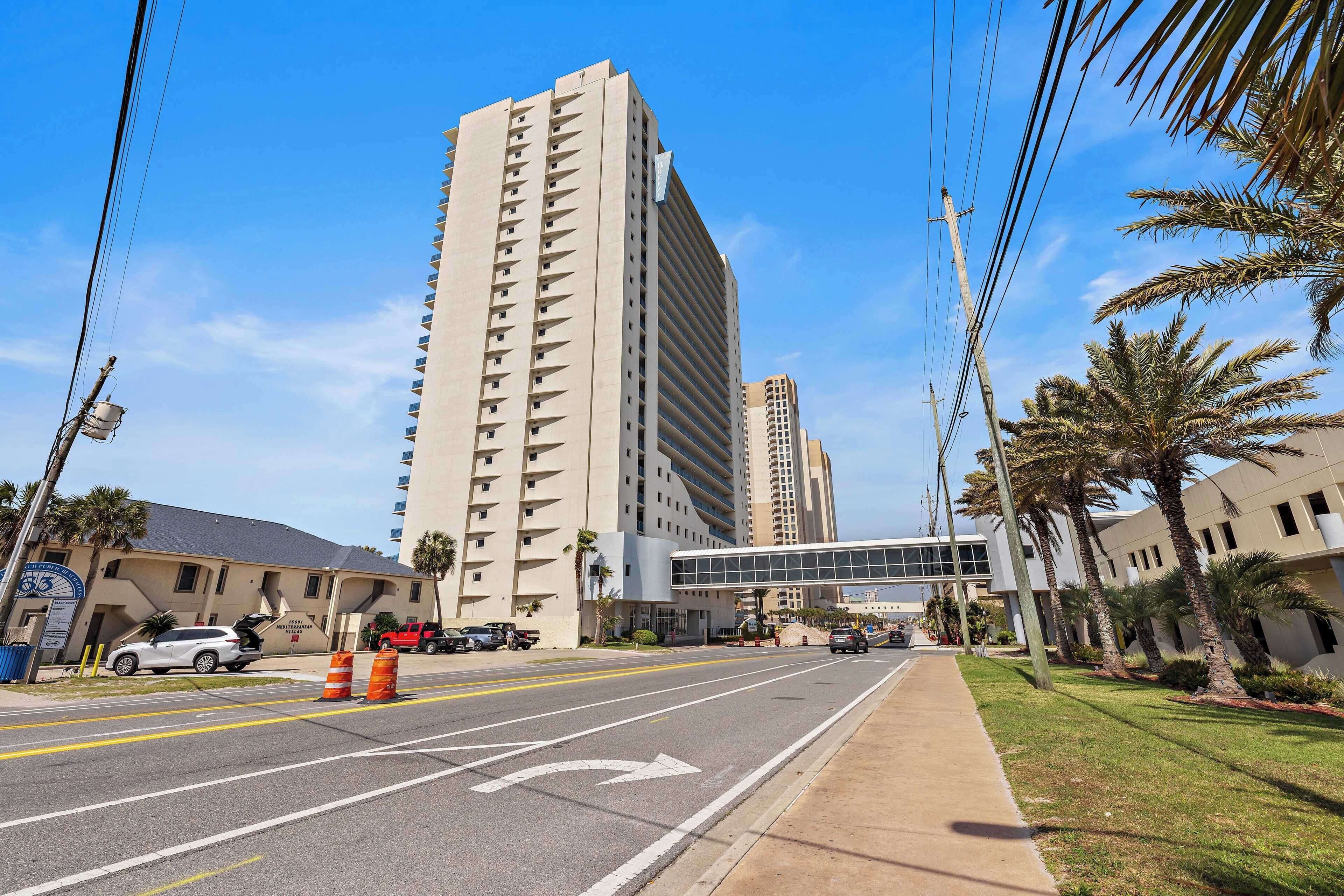 A multi-story hotel building with a modern design, a pedestrian overpass, and a clear sky.