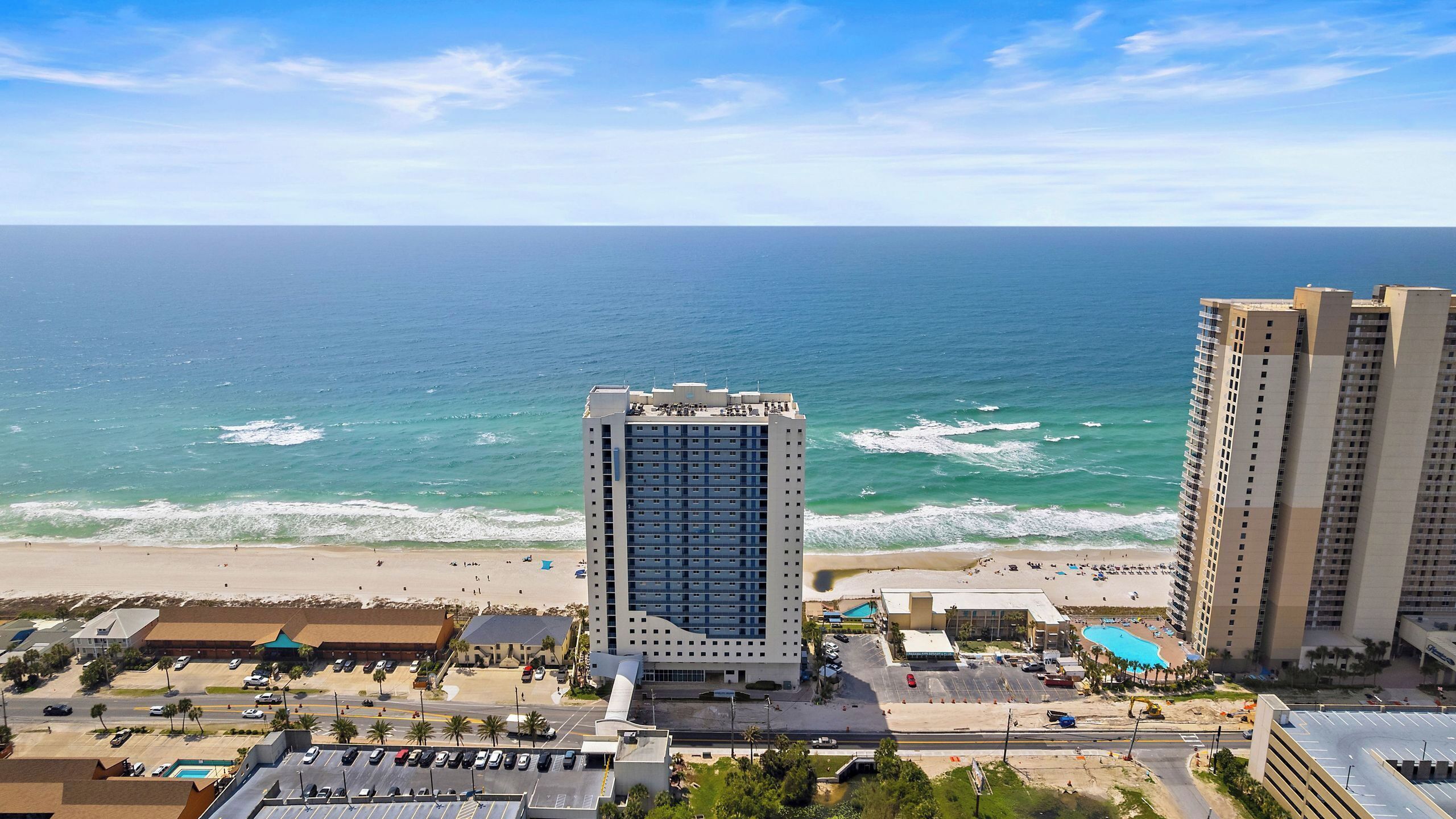 A coastal hotel with a view of the ocean, a parking lot, and a beach.