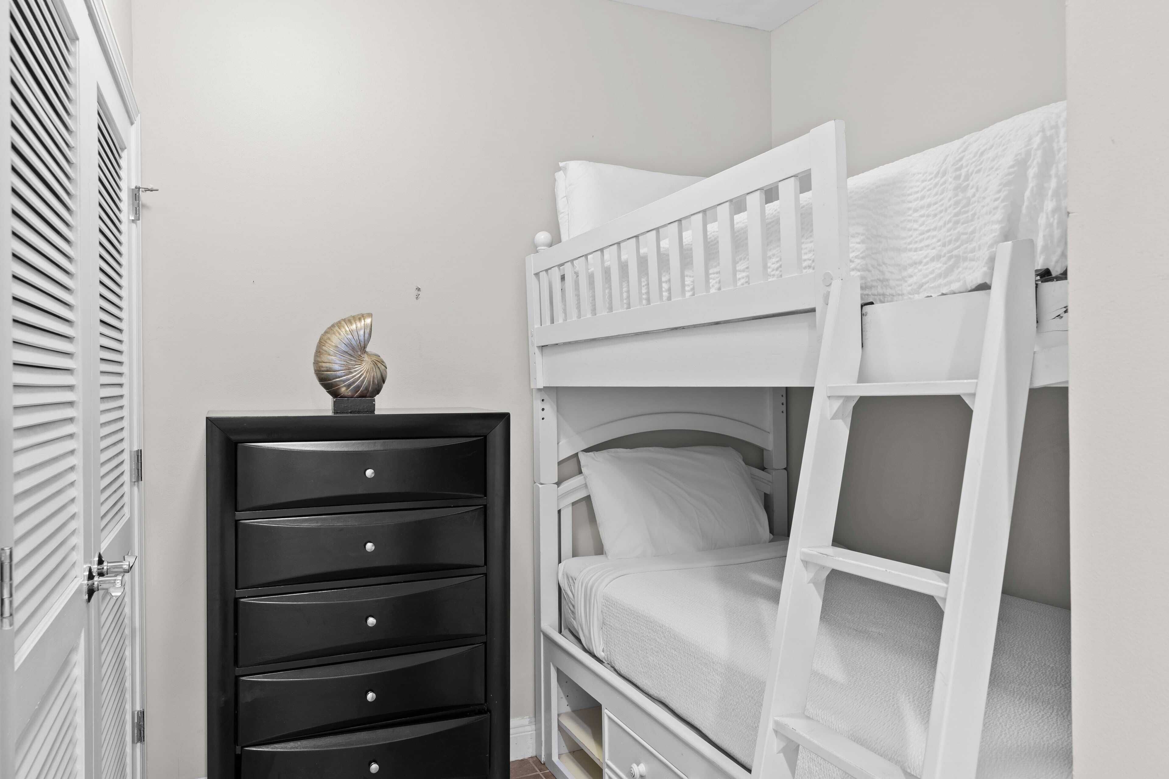 A bunk bed with a ladder, a dresser with drawers, and a door with louvered shutters.