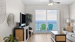A living room with a TV, wicker furniture, a balcony with chairs, and a view of the ocean. - Beachfront Stay w/ Resort Amenities & Gulf Views Sterling Breezing #506 (Panama City Beach)