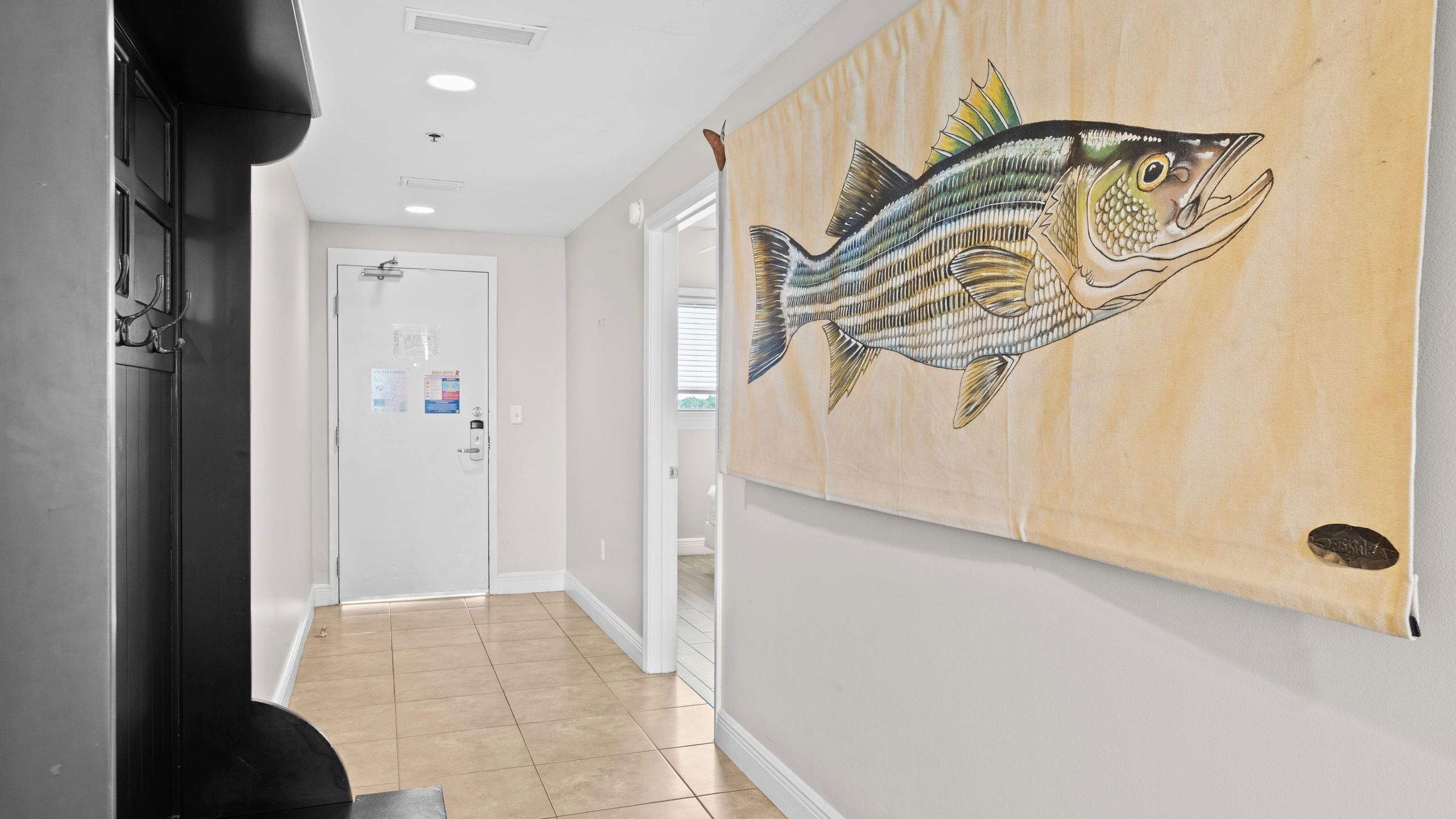 A hallway with a tiled floor, a door with a paper holder, and a large fish mural on the wall.