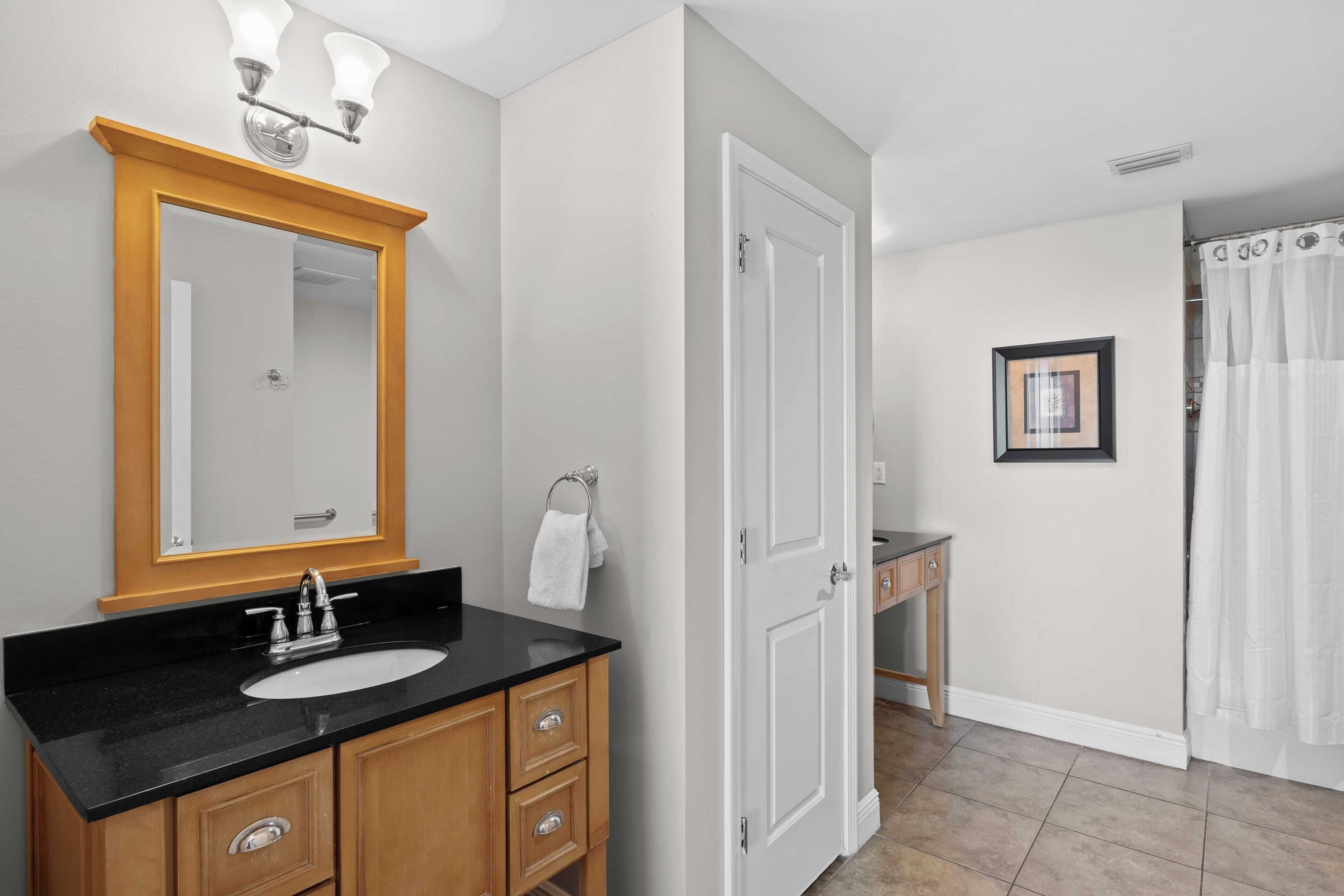 A bathroom with a black sink, wooden vanity, white door, and a framed picture on the wall.