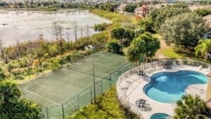 Ein Tennisplatz, umgeben von üppiger Vegetation und einem Schwimmbad.