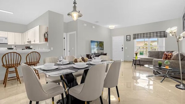 Eine moderne Küche mit weißen Schränken, ein Essbereich mit Tisch für vier Personen und ein Wohnzimmer mit Sofa und Couchtisch.