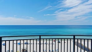 Vista a la playa desde un balcón con barandilla, cielo despejado y mar tranquilo.