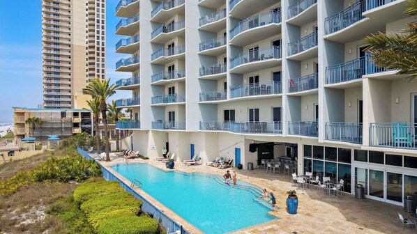 Ein Hotel mit Swimmingpool, mehreren Balkonen und Blick auf den Strand.
