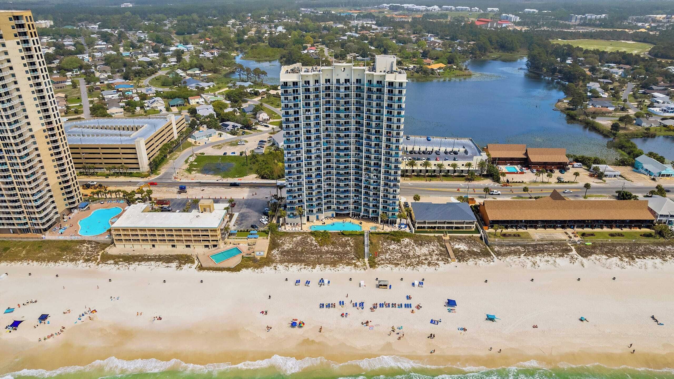 Un hôtel situé sur la côte, avec plusieurs étages, une piscine et un espace de plage équipé de chaises longues.