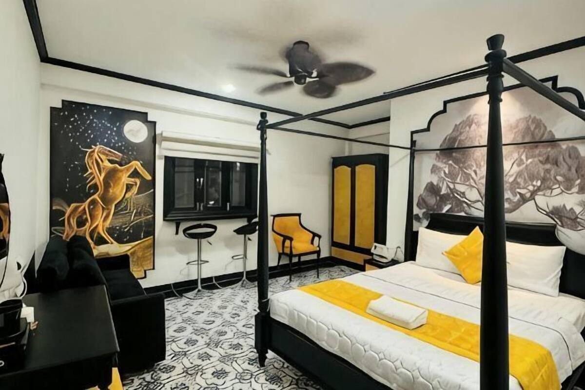 Ein Bett mit Baldachin, Deckenventilator, Schreibtisch mit Stuhl und Kunstwerke an den Wänden.