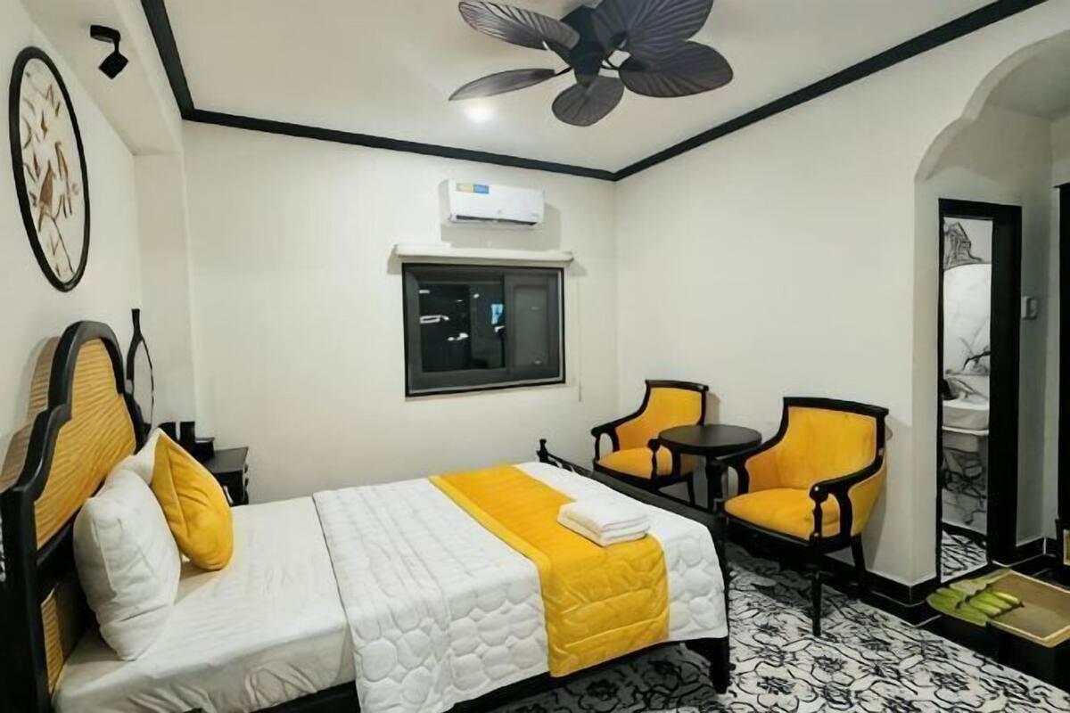 Ein Hotelzimmer mit Bett, Sessel, kleinem Tisch, Deckenventilator und Fenster.