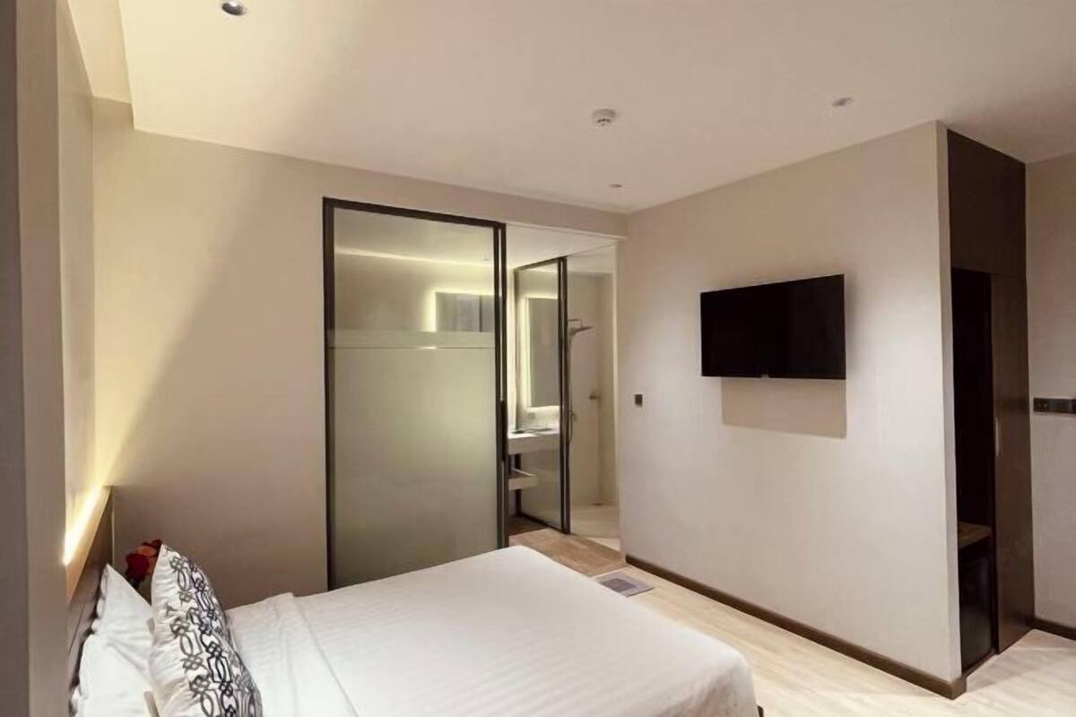 Une chambre d’hôtel moderne équipée d’un lit, d’une télévision, d’un miroir et d’une porte coulissante donnant accès à la salle de bain.