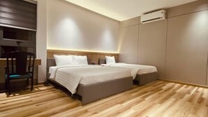 Un dormitorio moderno con suelo de madera, dos camas, una silla y un equipo de aire acondicionado.