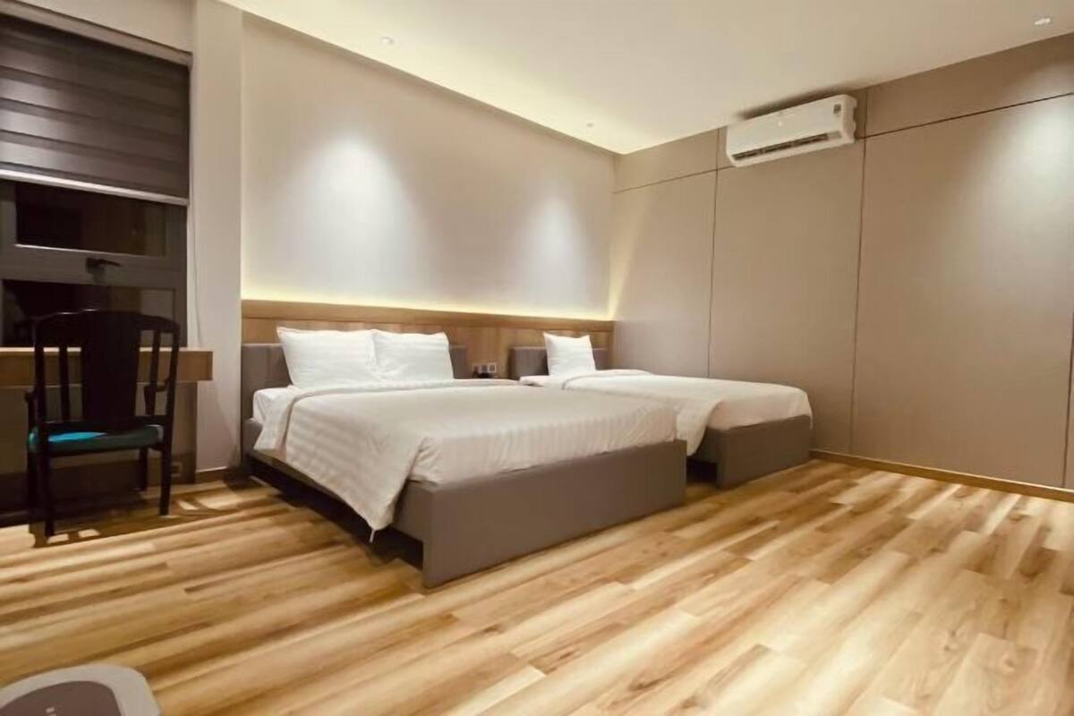 Une chambre moderne avec un plancher en bois, deux lits, une chaise et un appareil de climatisation.