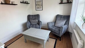 Uma sala de estar com dois poltronas listradas, uma mesa de centro clara e um letreiro na parede com a inscrição 'Good Vibes Only'.